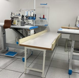 Bancone passalavoro ML.2 CPT di sponde e telaio in ferro, fotografato vicino a due postazioni di lavoro con macchine da cucire professionali